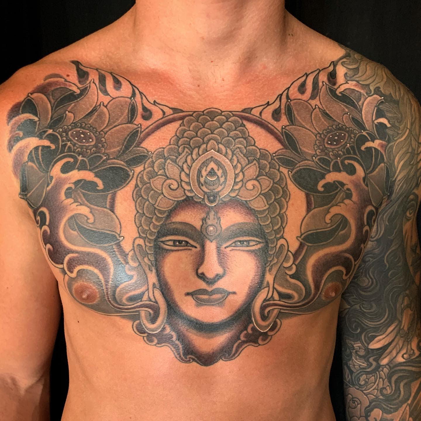 Chest tattoo features Buddha with ornate decorations, flanked by dark floral designs